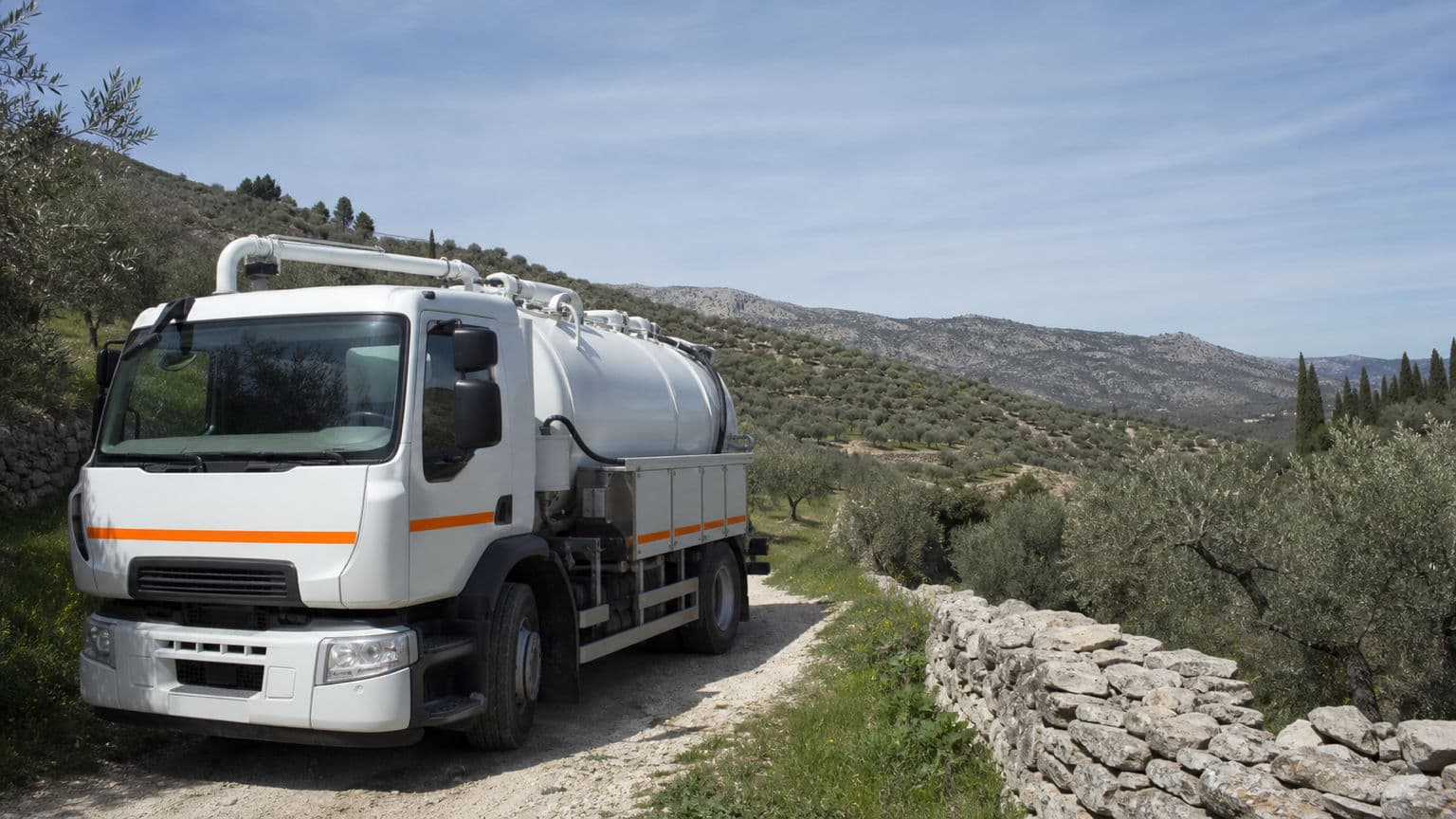 Camion hydrocureur d'Assainissement Vaucluse stationné au bord d'une oliveraie près de Nyons