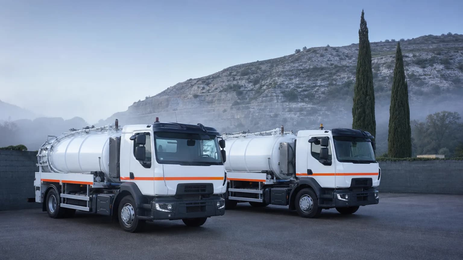 Deux camions hydrocureurs garés côte à côte dans la cour du dépôt à l'aube