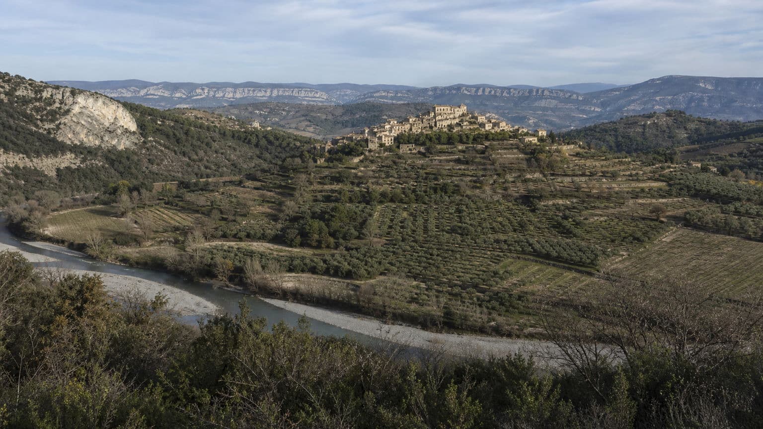 Vallée de la Drôme provençale vue depuis les hauteurs, oliveraies en terrasses et village perché